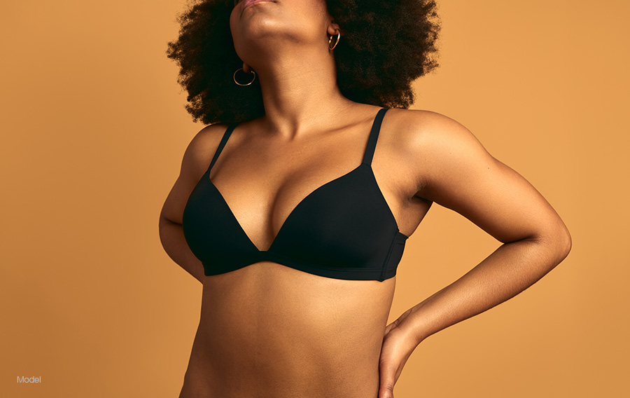 cropped image of a woman in a black bra against a tan background.